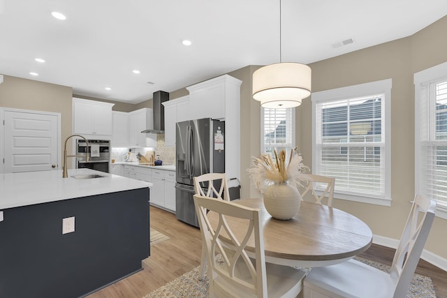 kitchen with decorative light fixtures, sink, white cabinets, stainless steel appliances, and wall chimney range hood