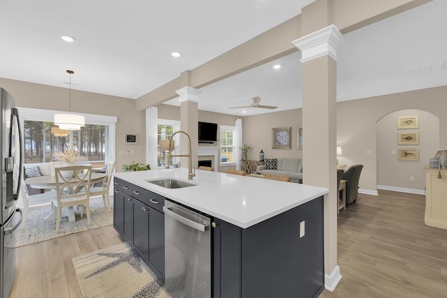 kitchen featuring sink, appliances with stainless steel finishes, hanging light fixtures, an island with sink, and light wood-type flooring