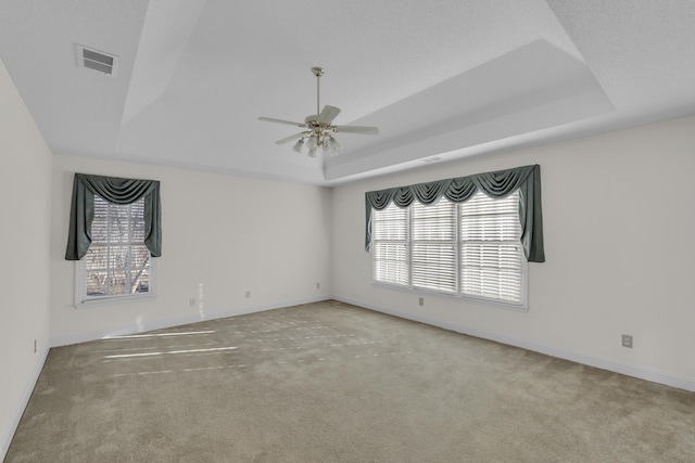 unfurnished room with a tray ceiling, light colored carpet, and ceiling fan