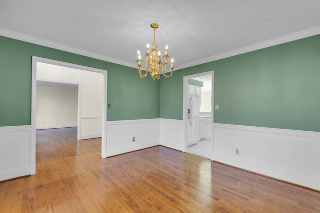 spare room featuring ornamental molding, a chandelier, a textured ceiling, and light wood-type flooring