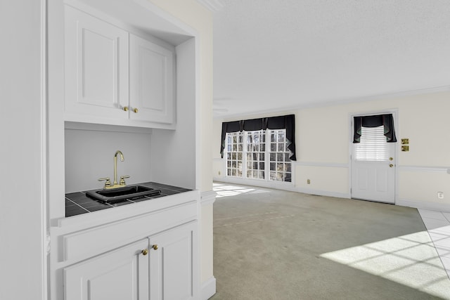 bar featuring white cabinetry, light colored carpet, sink, and a textured ceiling