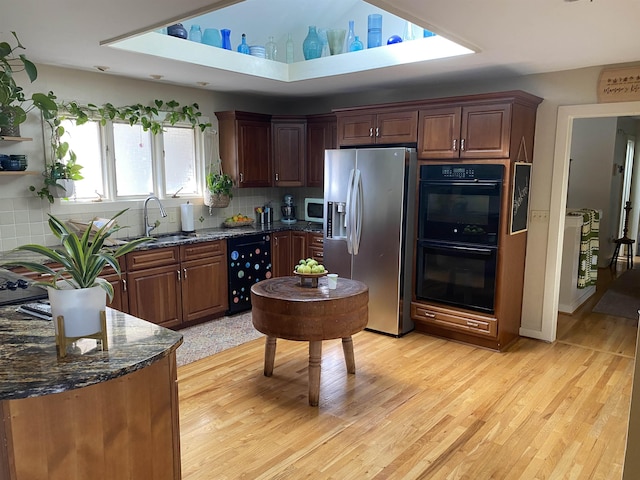 kitchen with sink, wine cooler, dark stone counters, stainless steel appliances, and light wood-type flooring