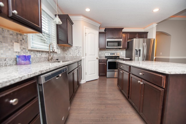 kitchen featuring stainless steel appliances, sink, light stone counters, and decorative light fixtures