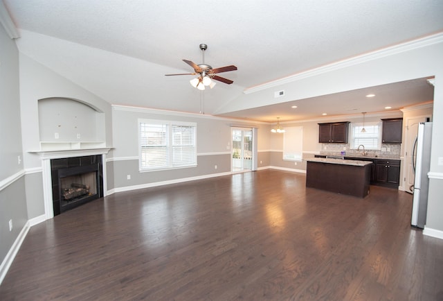 unfurnished living room featuring vaulted ceiling, ornamental molding, dark hardwood / wood-style floors, a fireplace, and ceiling fan with notable chandelier