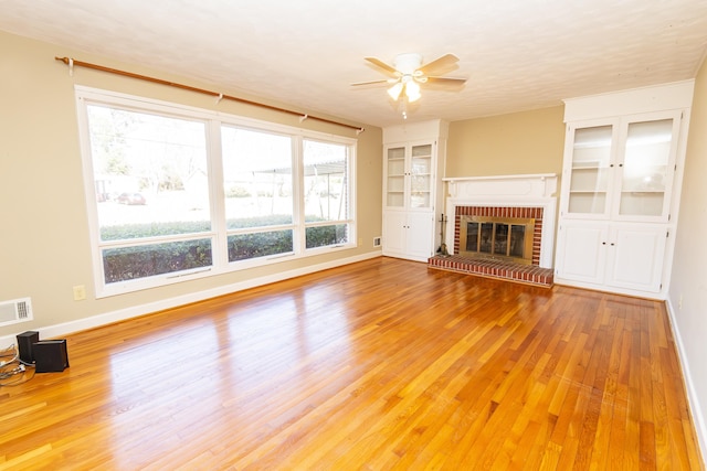 unfurnished living room with ceiling fan, built in shelves, a fireplace, and light hardwood / wood-style flooring