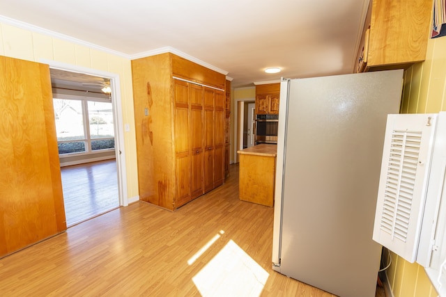 kitchen featuring refrigerator, stainless steel oven, ceiling fan, crown molding, and light wood-type flooring