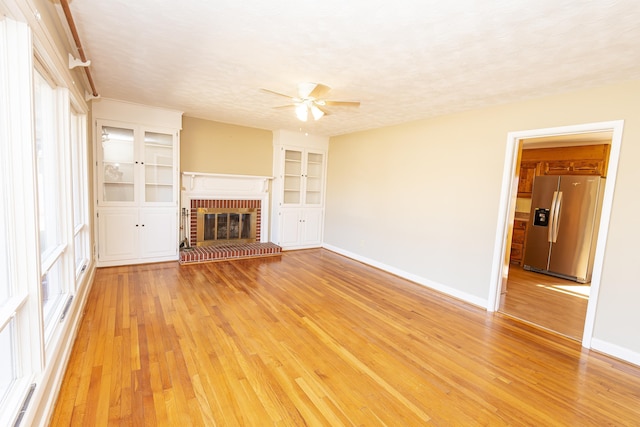 unfurnished living room with a brick fireplace, a textured ceiling, and light hardwood / wood-style floors