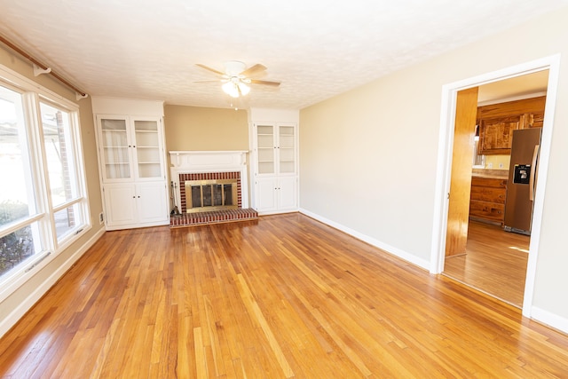 unfurnished living room featuring a fireplace, built in shelves, light hardwood / wood-style flooring, and a textured ceiling