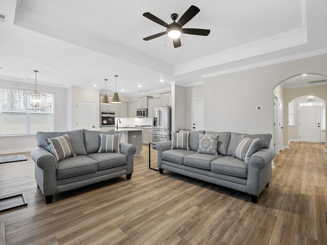 living room with a raised ceiling, ornamental molding, hardwood / wood-style flooring, and ceiling fan with notable chandelier