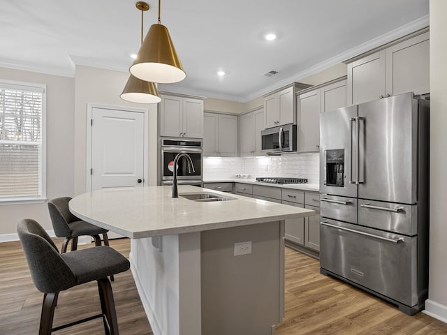 kitchen featuring sink, decorative light fixtures, ornamental molding, stainless steel appliances, and a kitchen island with sink