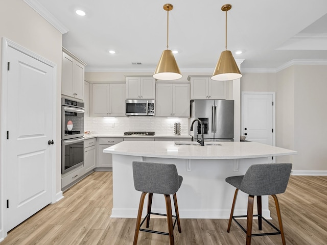 kitchen with sink, hanging light fixtures, ornamental molding, stainless steel appliances, and a center island with sink