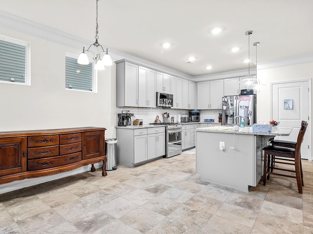 kitchen featuring appliances with stainless steel finishes, backsplash, hanging light fixtures, light stone counters, and a center island with sink