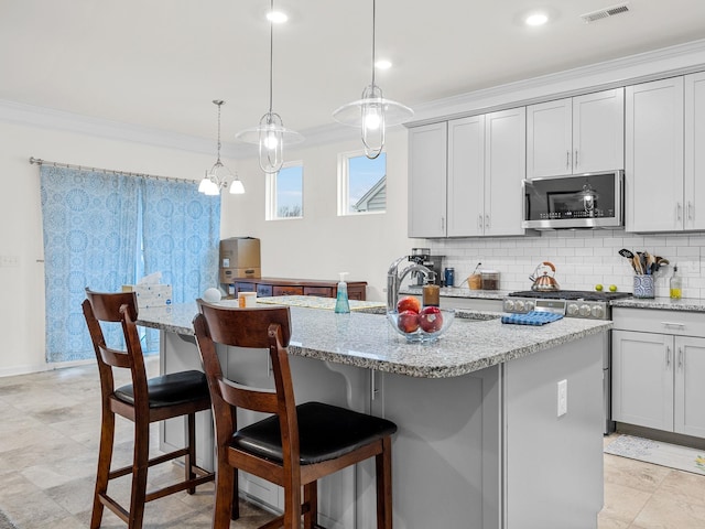 kitchen with crown molding, appliances with stainless steel finishes, pendant lighting, light stone countertops, and a kitchen island with sink