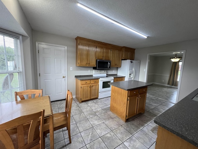 kitchen featuring a kitchen island, light tile patterned floors, a textured ceiling, and white appliances