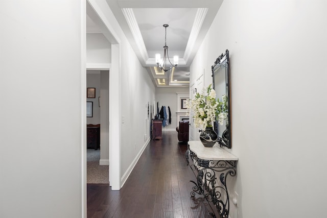 hall with crown molding, dark hardwood / wood-style flooring, a raised ceiling, and a chandelier