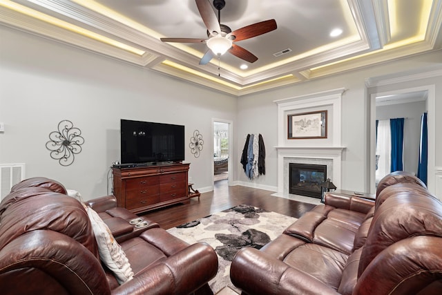 living room featuring dark hardwood / wood-style floors, a fireplace, ceiling fan, a raised ceiling, and crown molding