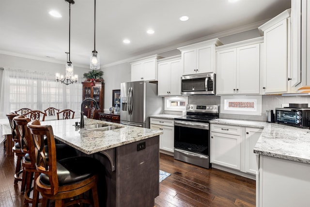 kitchen with white cabinetry, stainless steel appliances, decorative light fixtures, and an island with sink