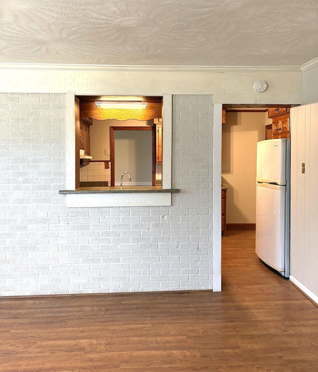 interior space featuring brick wall, hardwood / wood-style floors, sink, ornamental molding, and a textured ceiling