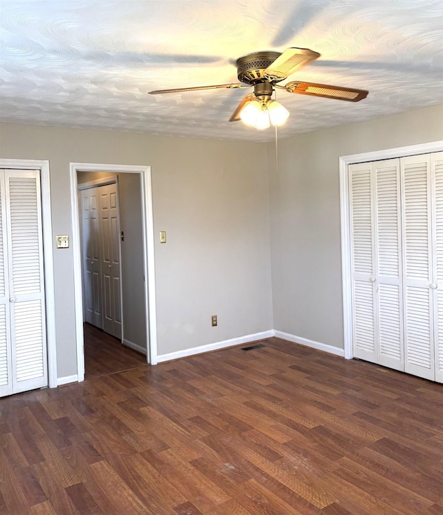 unfurnished bedroom featuring dark hardwood / wood-style flooring, two closets, and ceiling fan