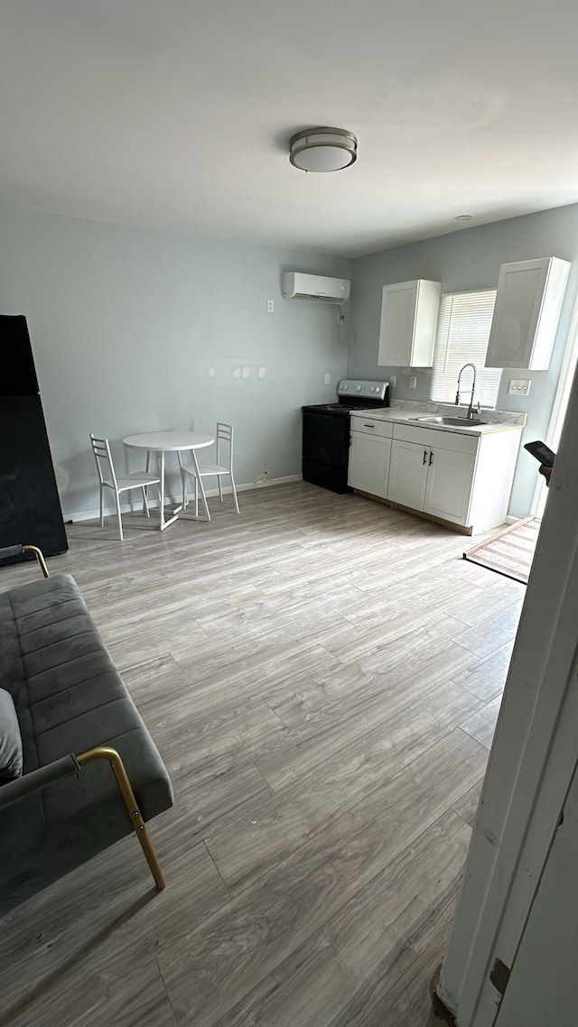 kitchen with sink, electric range oven, a wall mounted air conditioner, white cabinets, and light wood-type flooring