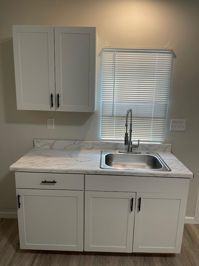 kitchen with light stone countertops, sink, hardwood / wood-style floors, and white cabinets