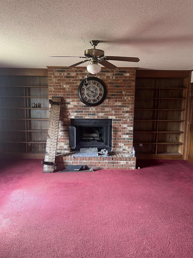 unfurnished living room featuring carpet, ceiling fan, a brick fireplace, a textured ceiling, and built in shelves