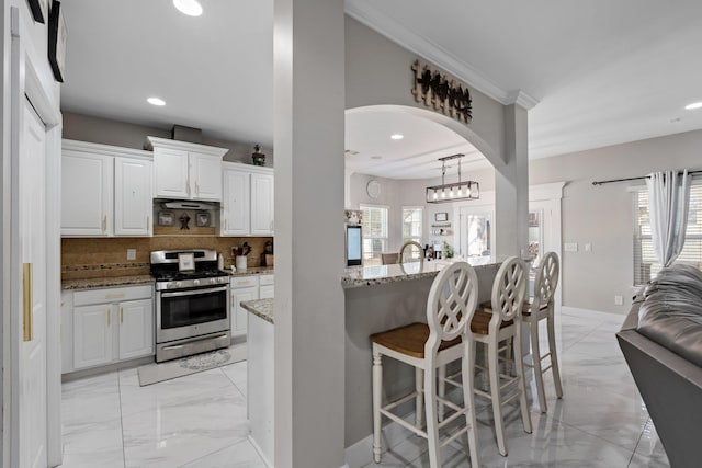 kitchen with a kitchen bar, stainless steel gas range, light stone counters, decorative backsplash, and white cabinets