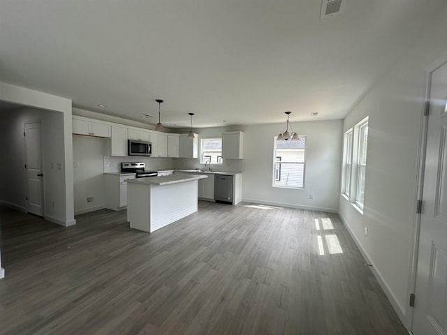 kitchen with sink, white cabinetry, hanging light fixtures, stainless steel appliances, and a kitchen island