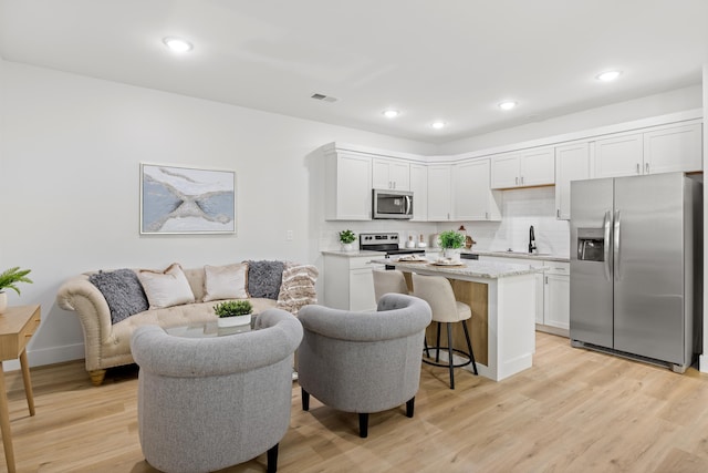 kitchen featuring light wood-type flooring, appliances with stainless steel finishes, a kitchen island, white cabinets, and backsplash