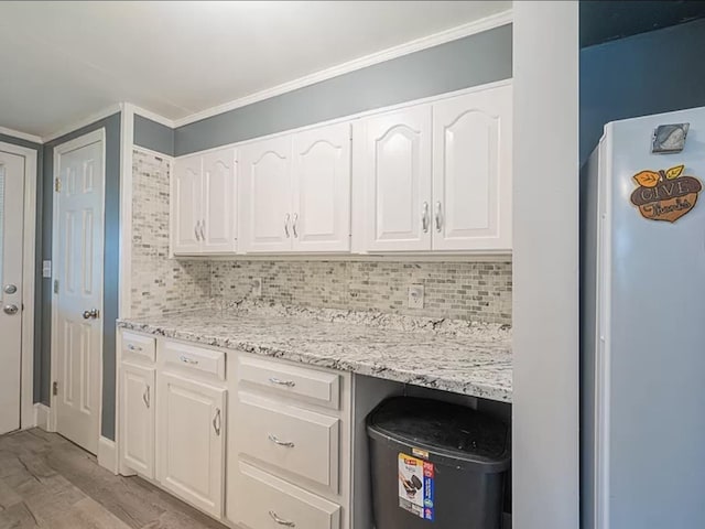 kitchen featuring white fridge, light stone countertops, white cabinets, decorative backsplash, and light wood-type flooring