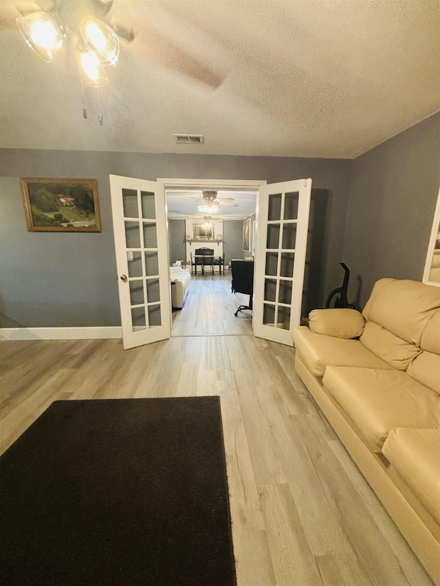 living room with french doors, ceiling fan, wood-type flooring, and a textured ceiling