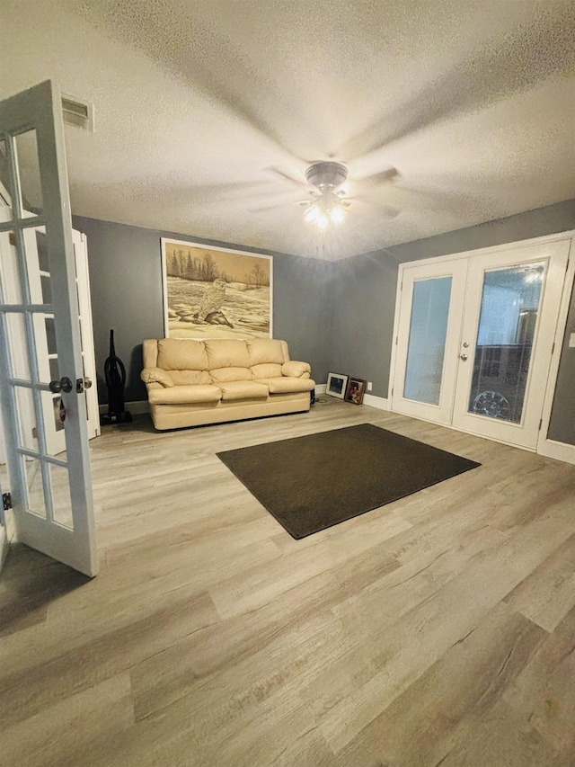 living room with ceiling fan, a textured ceiling, light wood-type flooring, and french doors