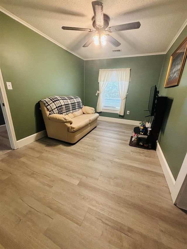 living area featuring ceiling fan, ornamental molding, wood-type flooring, and a textured ceiling