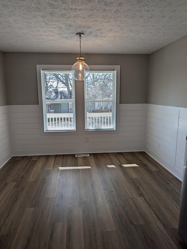 unfurnished dining area featuring a wealth of natural light, dark wood-type flooring, and a textured ceiling