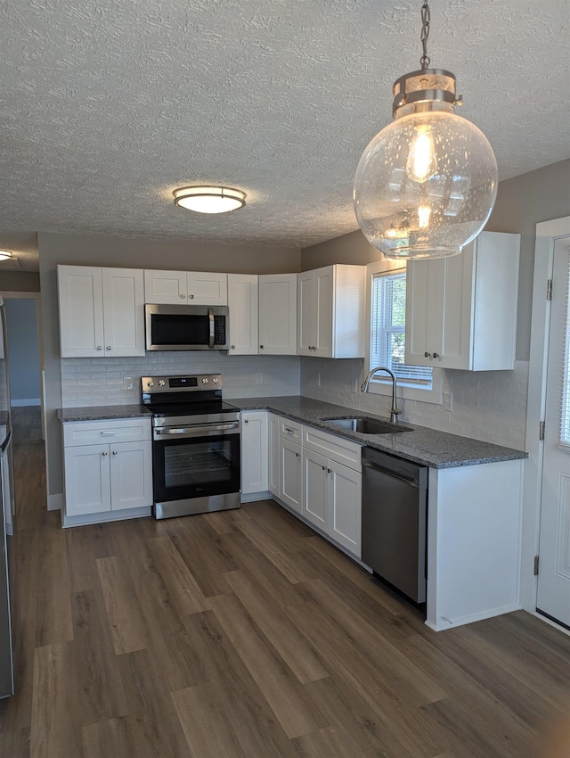 kitchen featuring white cabinetry, stainless steel appliances, decorative light fixtures, sink, and dark wood-type flooring