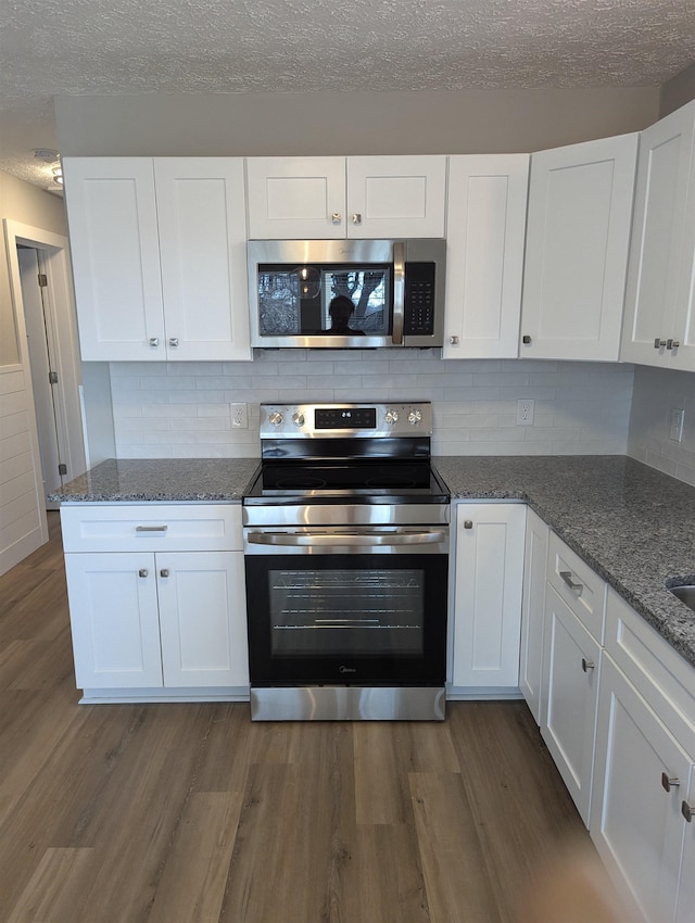 kitchen with appliances with stainless steel finishes, a textured ceiling, dark wood-type flooring, dark stone countertops, and white cabinets