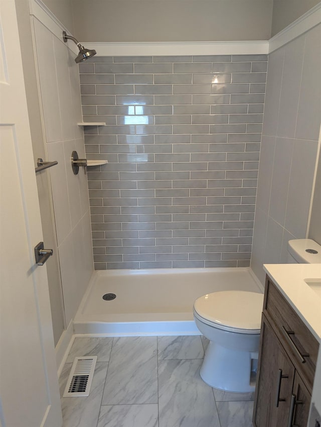 bathroom with a tile shower, vanity, and toilet