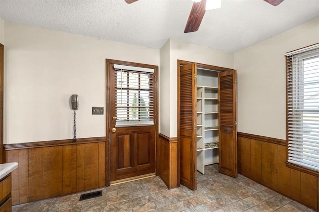 interior space with ceiling fan, wooden walls, and a textured ceiling