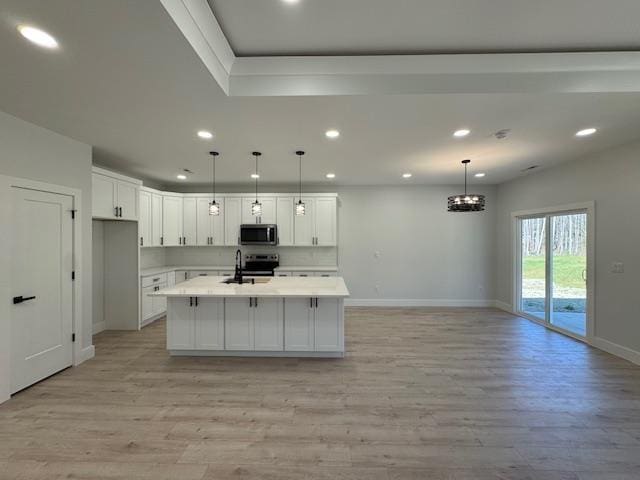 kitchen featuring a center island with sink, sink, pendant lighting, and white cabinets