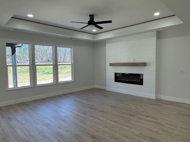 unfurnished living room featuring a large fireplace, light wood-type flooring, and a tray ceiling