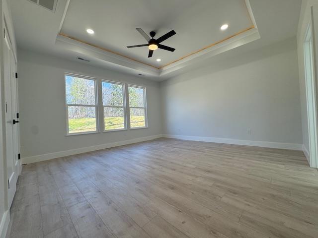 spare room featuring ceiling fan, ornamental molding, a tray ceiling, and light hardwood / wood-style flooring