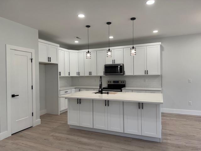 kitchen featuring pendant lighting, white cabinetry, a kitchen island with sink, and appliances with stainless steel finishes