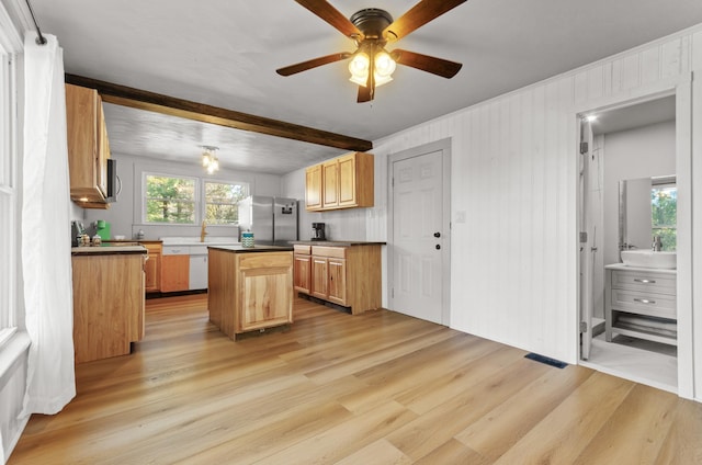 kitchen with appliances with stainless steel finishes, beam ceiling, light hardwood / wood-style floors, a kitchen island, and light brown cabinetry