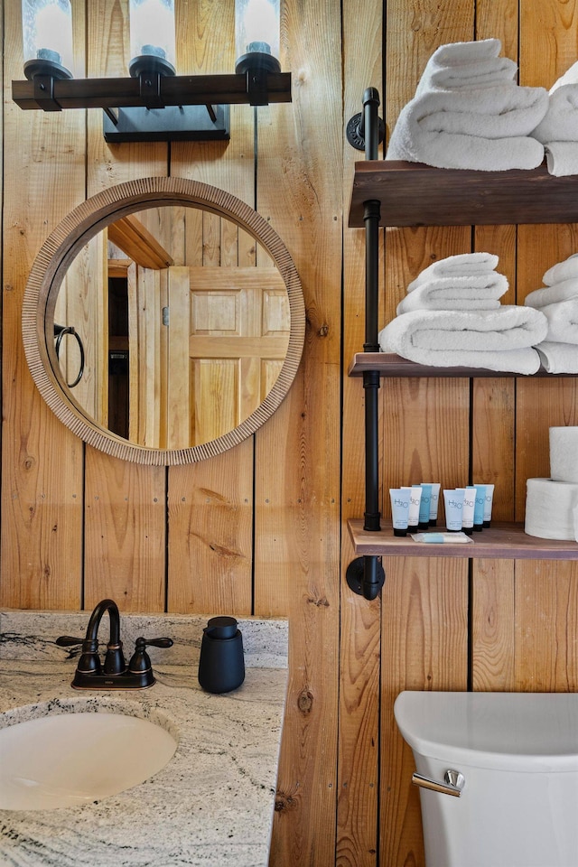 bathroom featuring wooden walls, vanity, and toilet