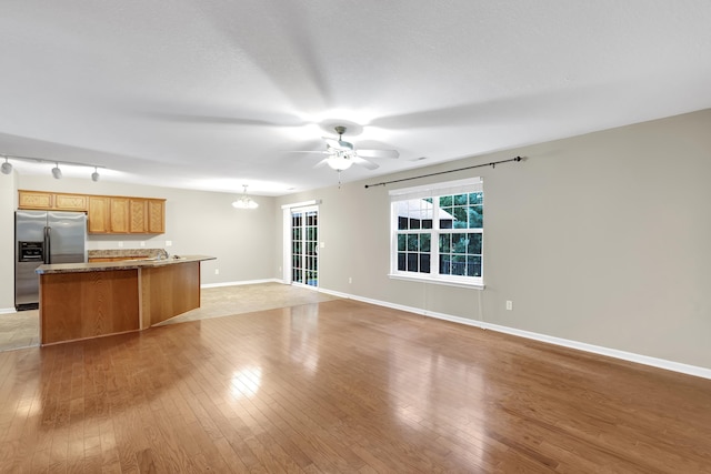 unfurnished living room featuring ceiling fan with notable chandelier and light hardwood / wood-style flooring