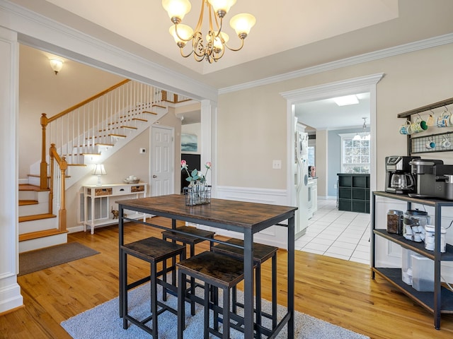 dining area with crown molding, a notable chandelier, light wood-type flooring, and a tray ceiling