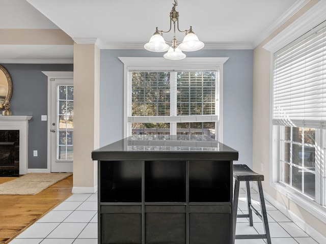 kitchen with pendant lighting, ornamental molding, light tile patterned floors, a high end fireplace, and an inviting chandelier