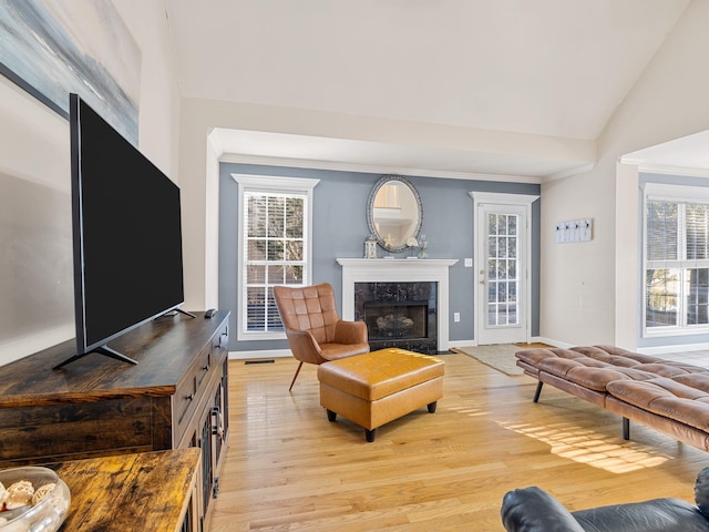 living room featuring light hardwood / wood-style flooring, crown molding, a fireplace, and vaulted ceiling