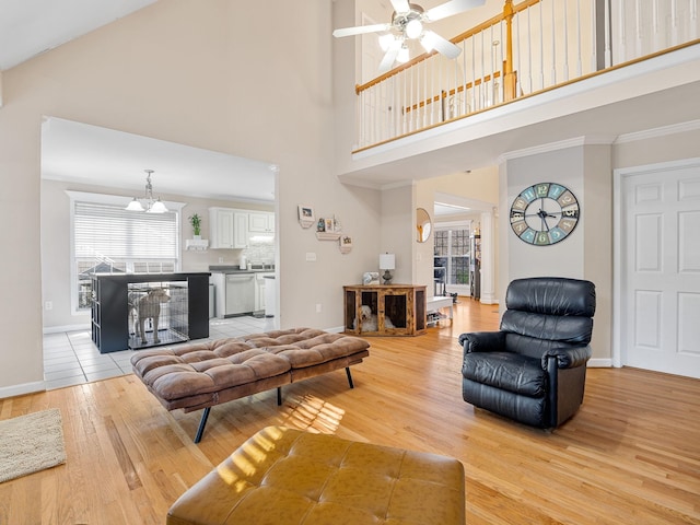 living room with ceiling fan with notable chandelier, light hardwood / wood-style flooring, ornamental molding, and a high ceiling