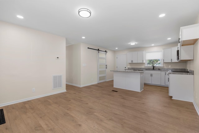 kitchen with sink, light wood-type flooring, a kitchen island, a barn door, and white cabinets